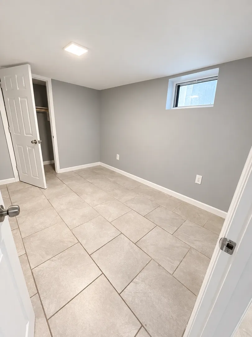 Bedroom with grey walls, white baseboards, a tile floor, a high horizontal window and an open closet with a shelf and rod.