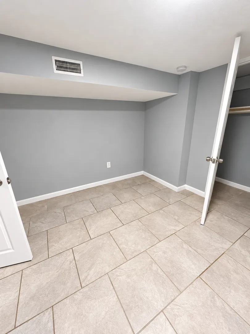 Second bedroom with grey walls, a ceiling soffit with a supply vent, a ceiling-mounted detector and an open closet.