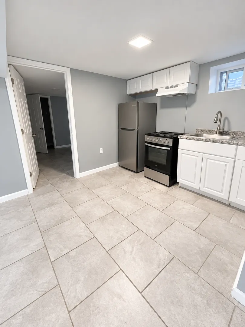 Kitchen with white upper and lower cabinets, a stainless refrigerator, a range with oven, a range hood, a sink with a gooseneck faucet, and a small window.